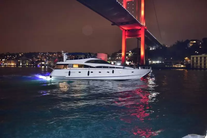 Yacht privato bianco in crociera notturna sotto il Ponte sul Bosforo illuminato