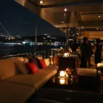 Bosphorus dinner cruise at night with a candlelit deck lounge and the illuminated 15 July Martyrs Bridge behind